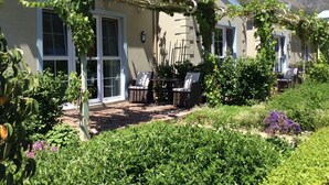 A house with a covered patio area, two outdoor chairs, and a garden with various plants and flowers.