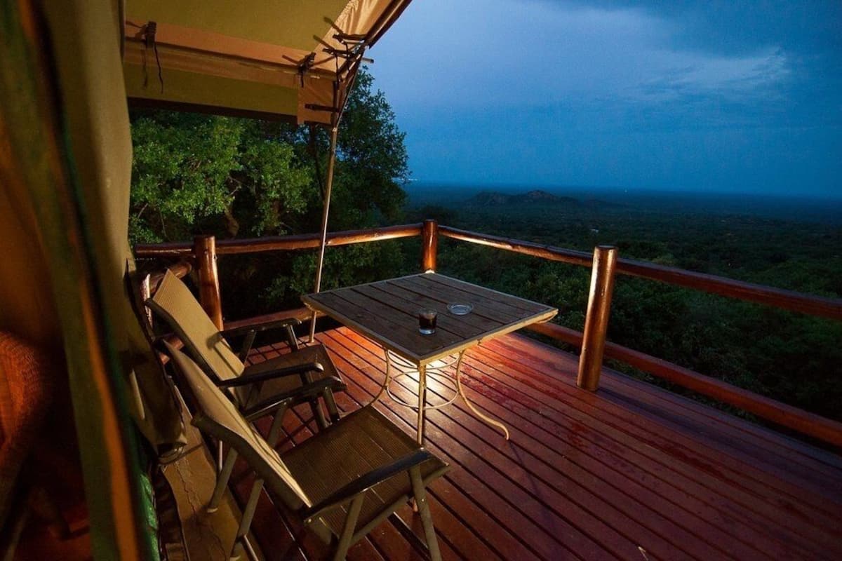Una terraza de madera con mesa y sillas, con vistas a un paisaje exuberante.