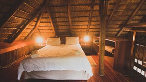 Un dormitorio acogedor en el ático, con techo de paja, una cama grande, lámparas de noche y muebles de madera.