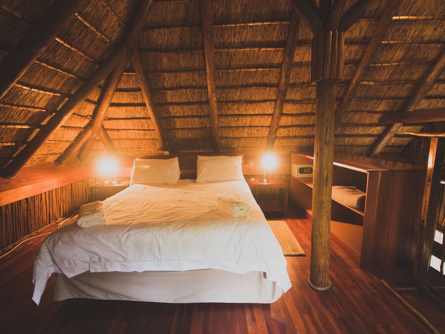 A cozy attic bedroom with a thatched roof, a large bed, bedside lamps, and wooden furniture.
