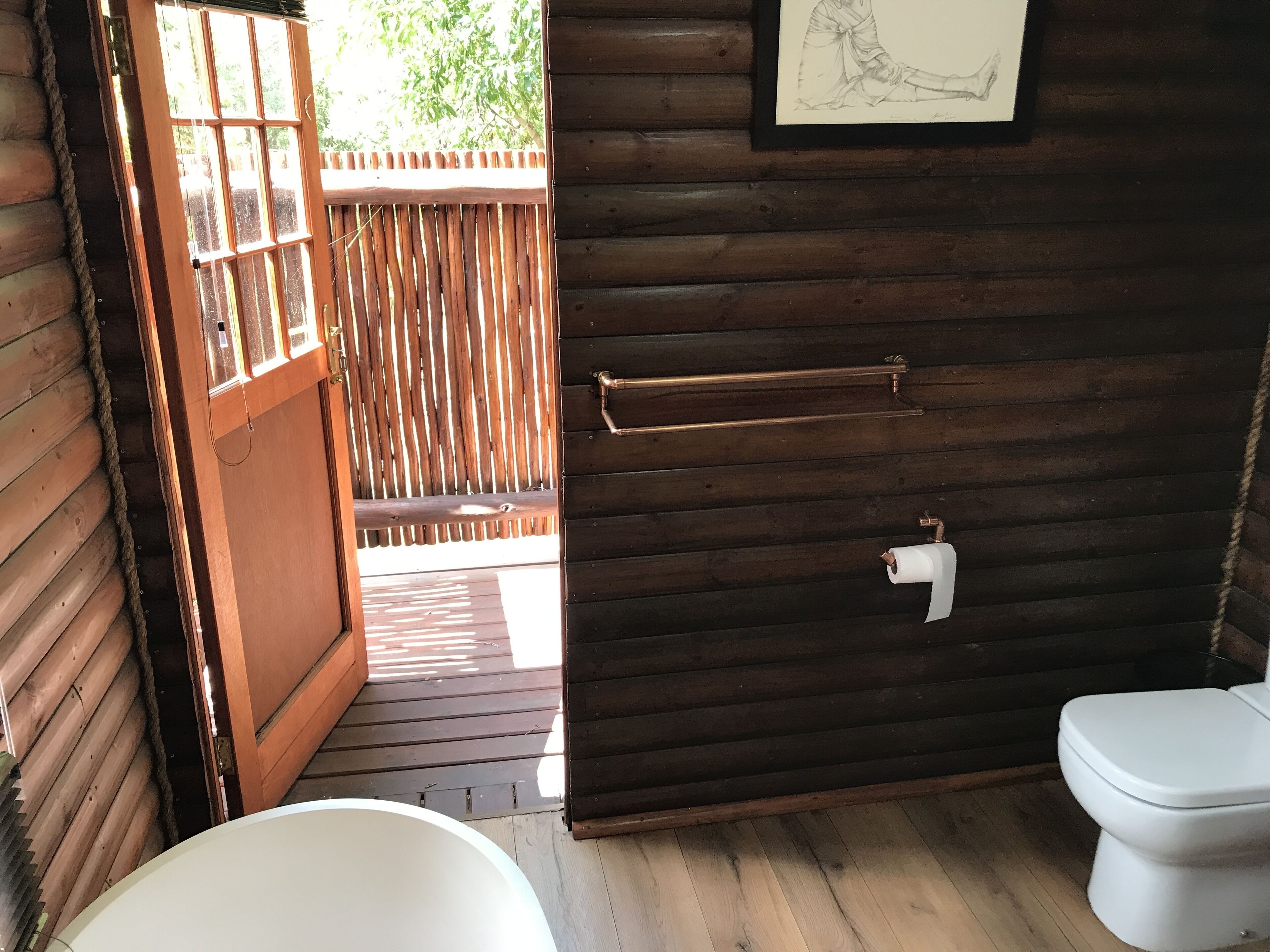 A wooden cabin bathroom with a toilet, a sink, and a shower area.