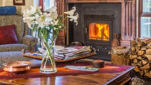 A cozy living room with a fireplace, a sofa, a coffee table with magazines and a vase of flowers. - Peace Valley Guesthouse (Napier)