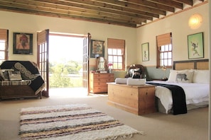 Quarto com cama, cómoda de madeira, cadeira e janela grande.