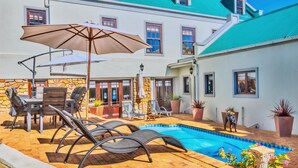 A poolside area with lounge chairs, a table, and umbrellas. - Peace Valley Guesthouse (Napier)