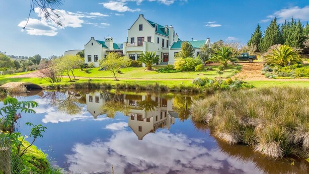 A large, white, two-story house with a green roof, surrounded by a well-maintained garden and a pond reflecting the house. - Peace Valley Guesthouse (Napier)