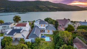 A large house with a swimming pool, surrounded by lush greenery and a view of a lake and hills. - The Knysna Belle (Knysna)