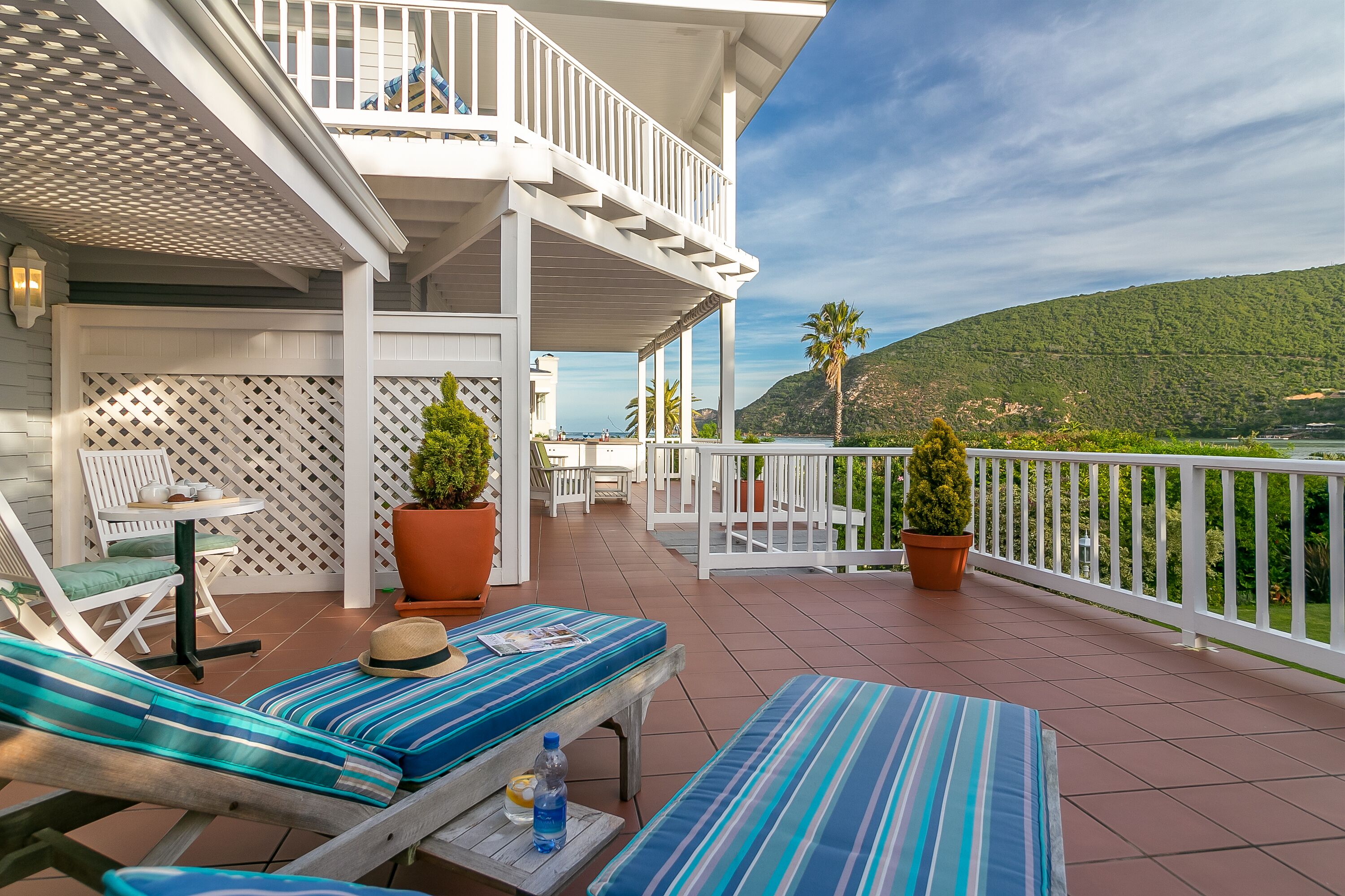 A balcony with striped cushions, a hat, and a bottle on a table.