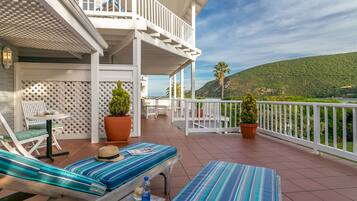 A balcony with striped cushions, a hat, and a bottle on a table.