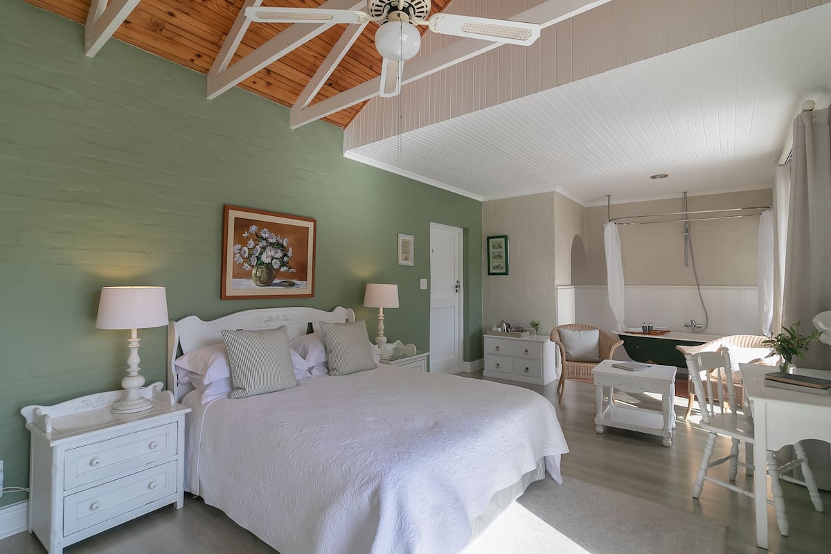 A bedroom with a bed, nightstands, a desk, and a shower area.