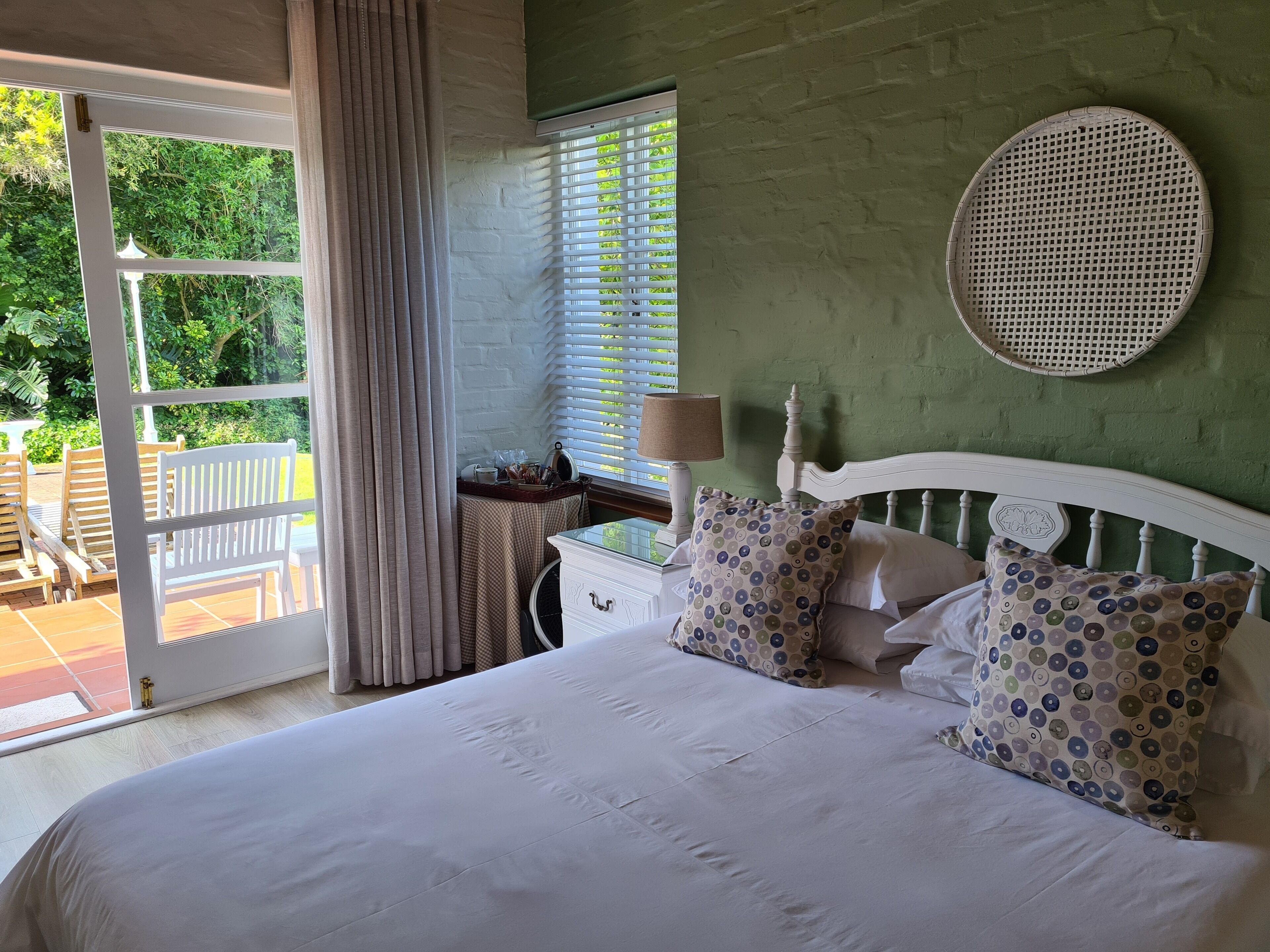 Une chambre à coucher avec un lit, une fenêtre avec des stores, un panier en osier et une table avec une lampe.