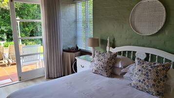 Une chambre à coucher avec un lit, une fenêtre avec des stores, un panier en osier et une table avec une lampe.