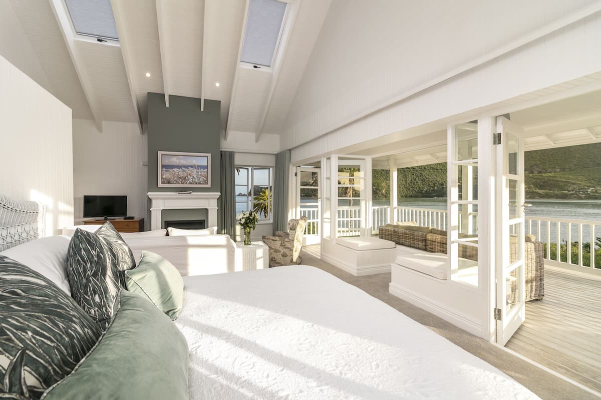 A bedroom with a large bed, a TV, a fireplace, and a balcony with a view of the water.