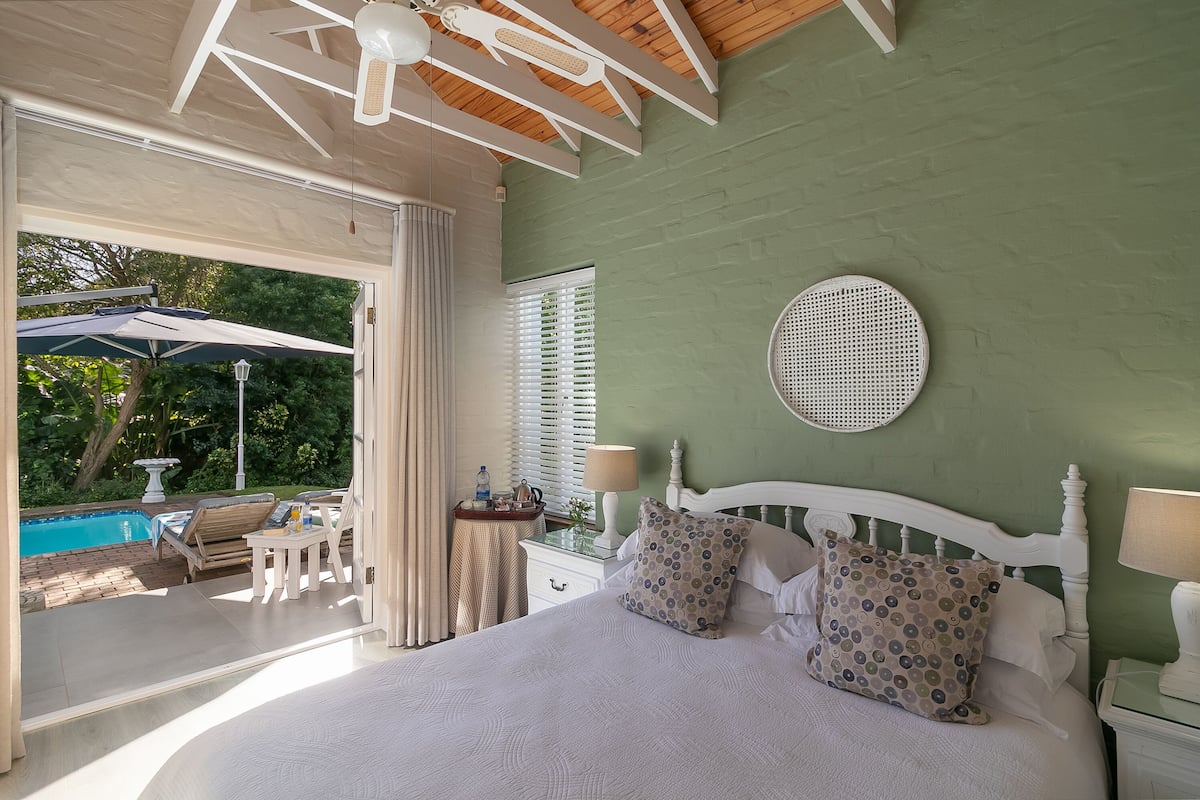A bedroom with a large bed, a view of an outdoor pool, and a green wall.