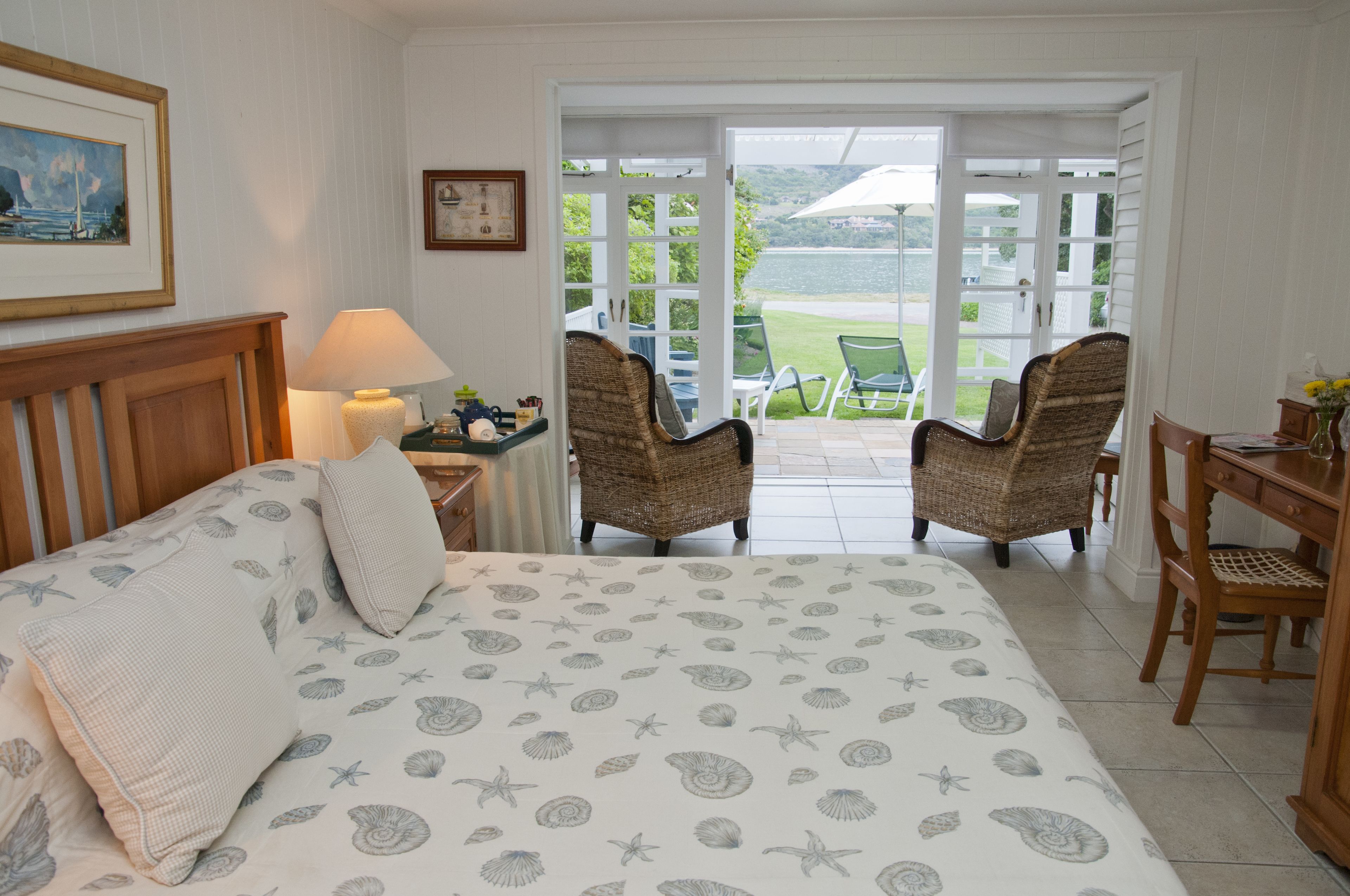 A bedroom with a bed, two wicker chairs, a wooden desk, and a view of the outdoors.