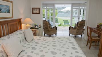 A bedroom with a bed, two wicker chairs, a wooden desk, and a view of the outdoors.