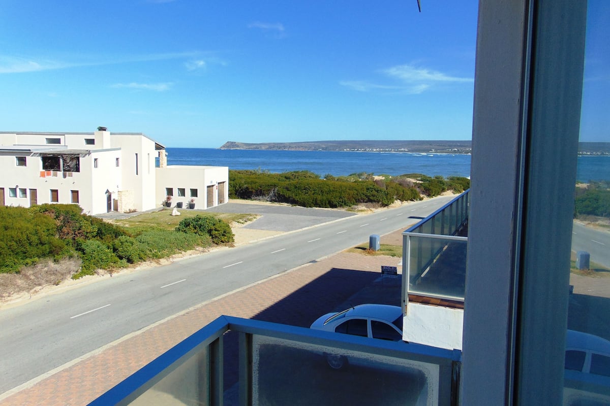 A coastal view from a balcony overlooking a road with a white building and a 'SOLD' sign.