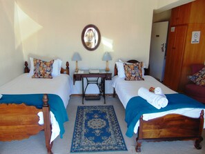 A hotel room with two single beds, a desk with a lamp, a sewing machine, and a mirror on the wall. - Whale Watchers Inn (Witsand)