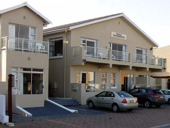 A two-story building with a sign reading "Whale Watchers Inn". There are cars parked in front and a ramp leading to the entrance. - Whale Watchers Inn (Witsand)