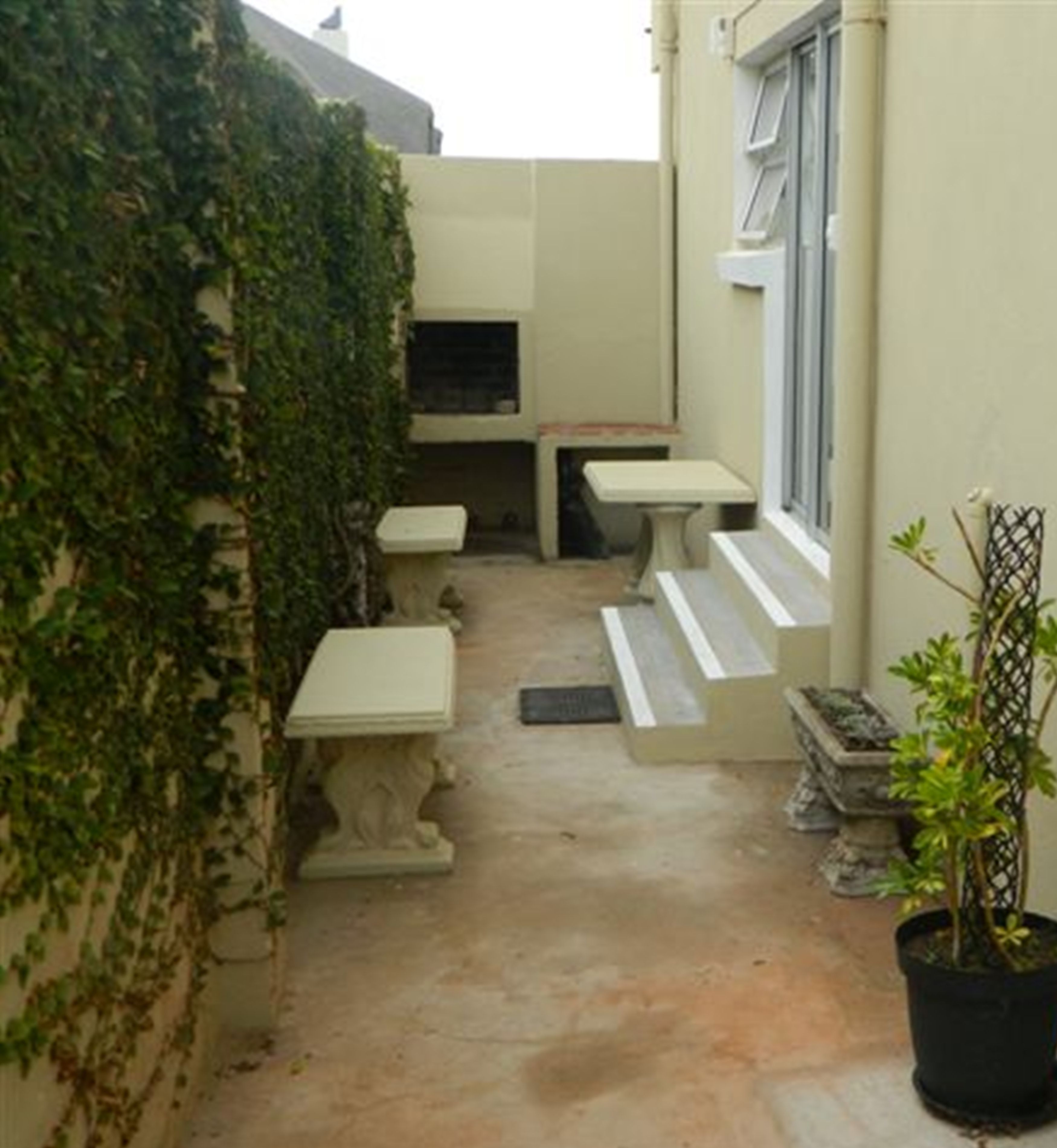 Un petit espace extérieur abrité, comprenant un banc, une table et un pot de fleurs.
