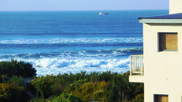 A coastal view with a building in the foreground and a boat in the distance.