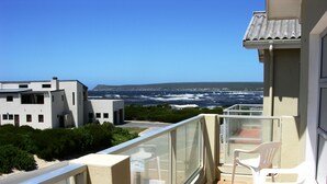 A balcony with a view of the ocean, white plastic chairs, and a tiled floor.