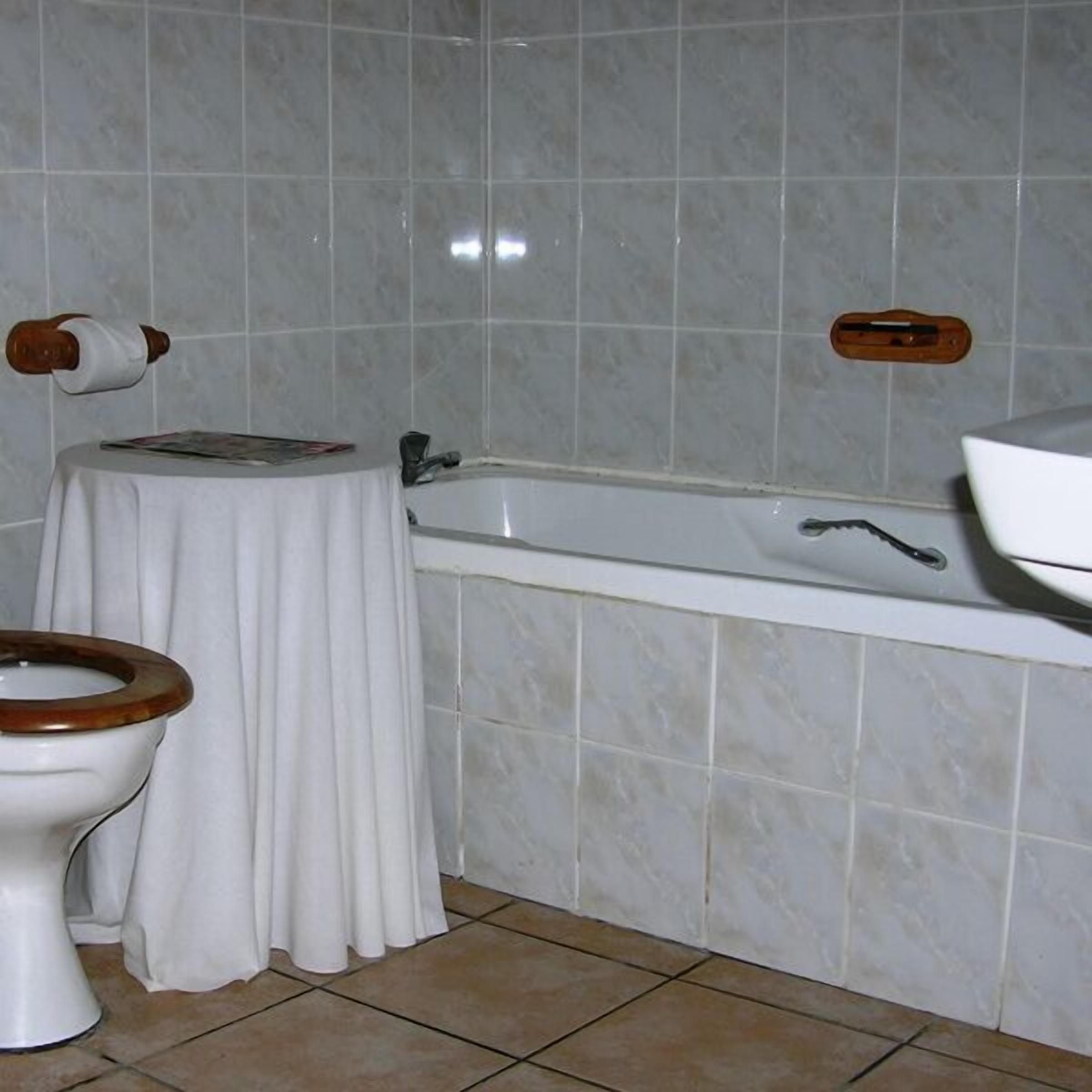 Une salle de bain comprenant des toilettes, une petite table avec un magazine, une baignoire et un espace douche.