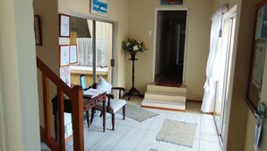A hallway with a staircase leading to a door, a dining area with a table and chairs, and a small plant.