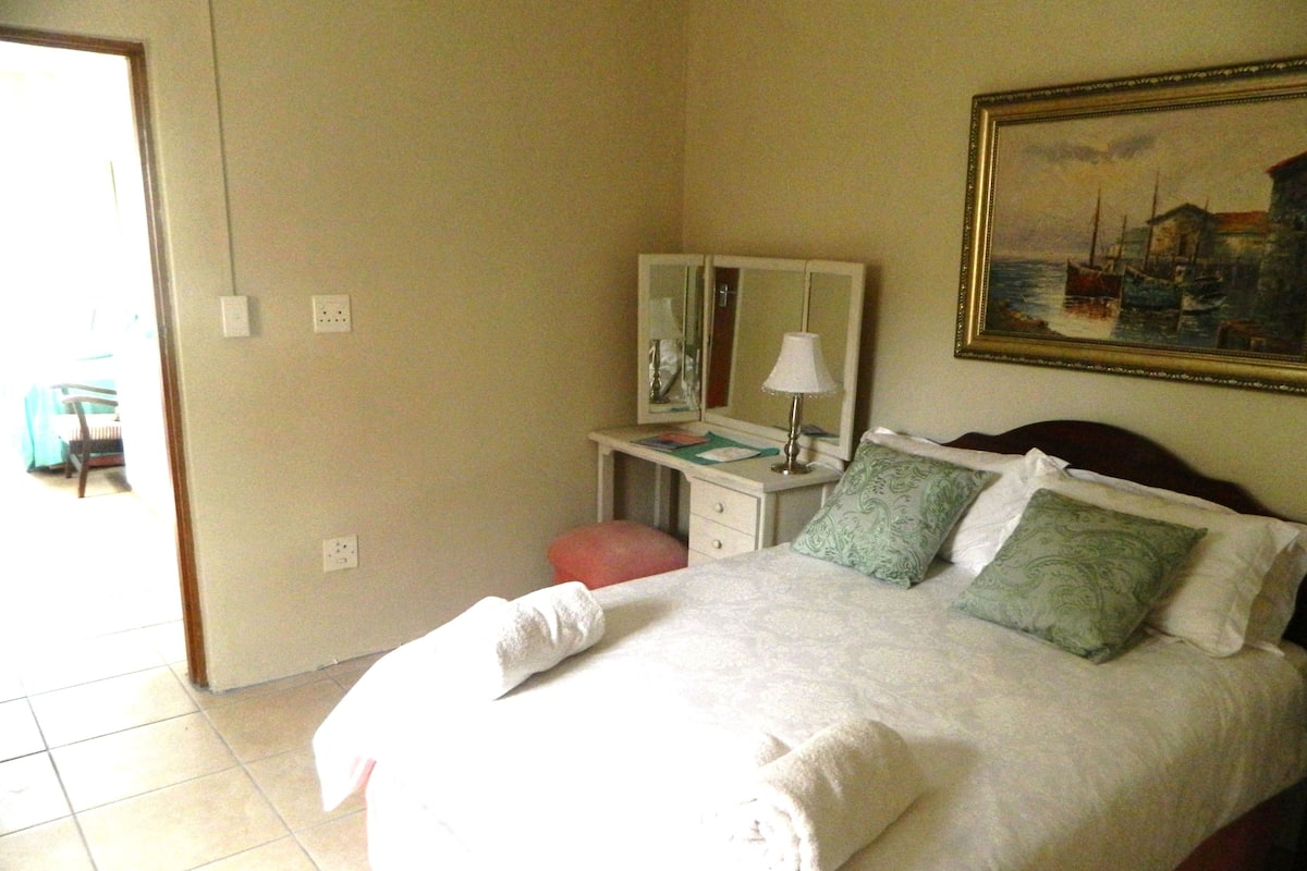 A bedroom with a bed, a bedside table with a lamp, a mirror, and a painting on the wall.