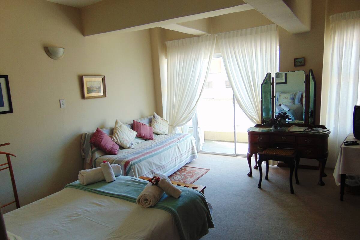 A hotel room with two beds, a desk, a chair, a mirror, and a television.