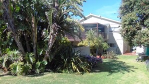 A two-story building with a covered patio area, surrounded by lush tropical plants and a well-maintained lawn.