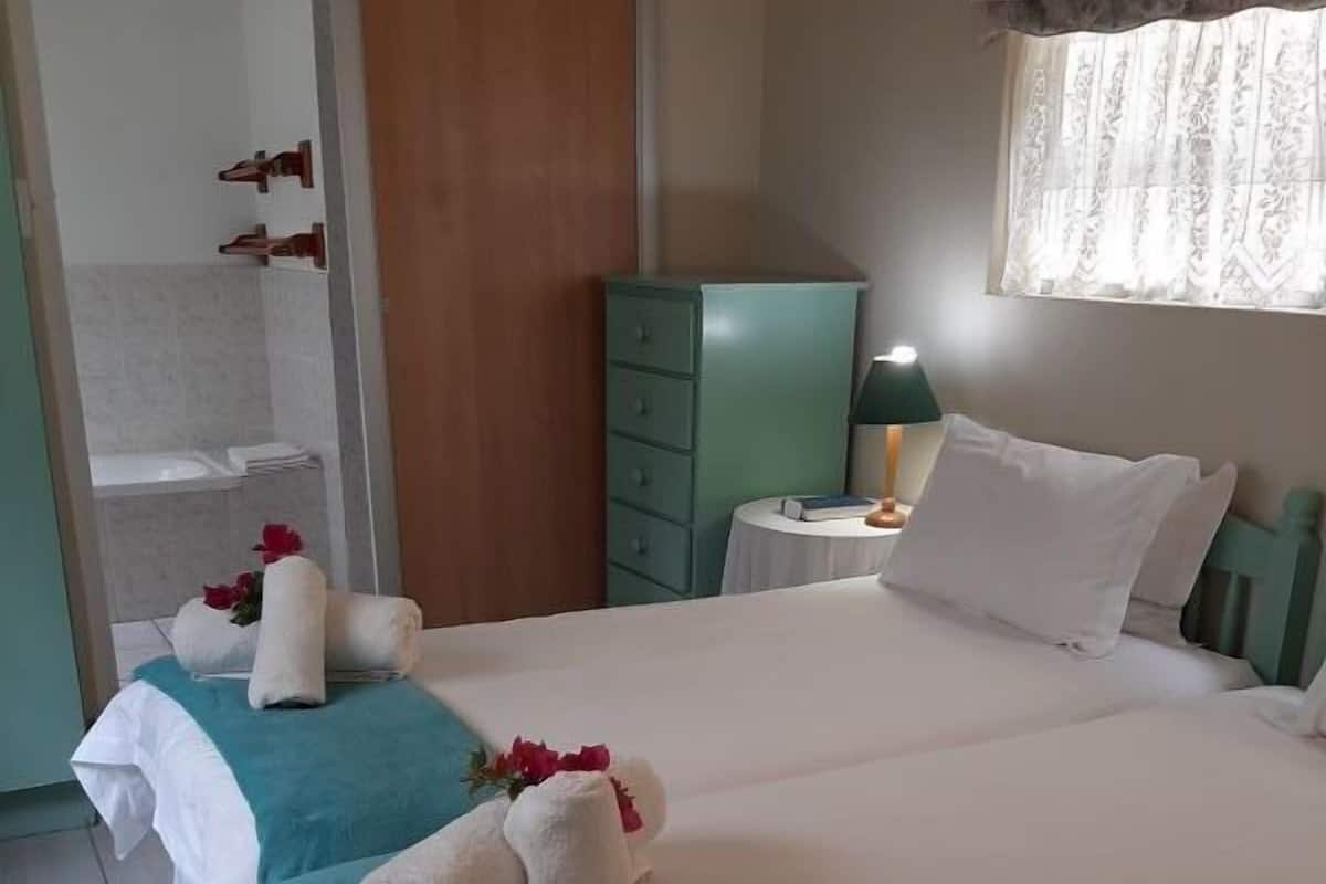 A neatly made bed with white and teal bedding, a nightstand with a lamp, and a green dresser.