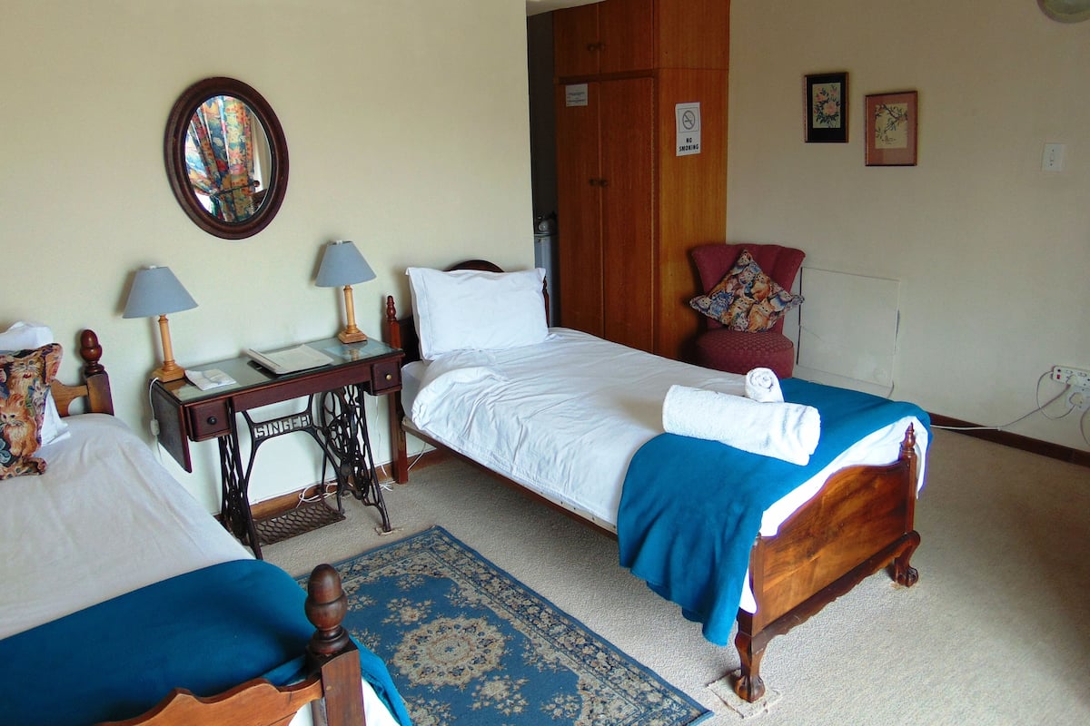 A hotel room with two single beds, a desk with a lamp, a chair, a mirror, and a door with a 'No Smoking' sign.