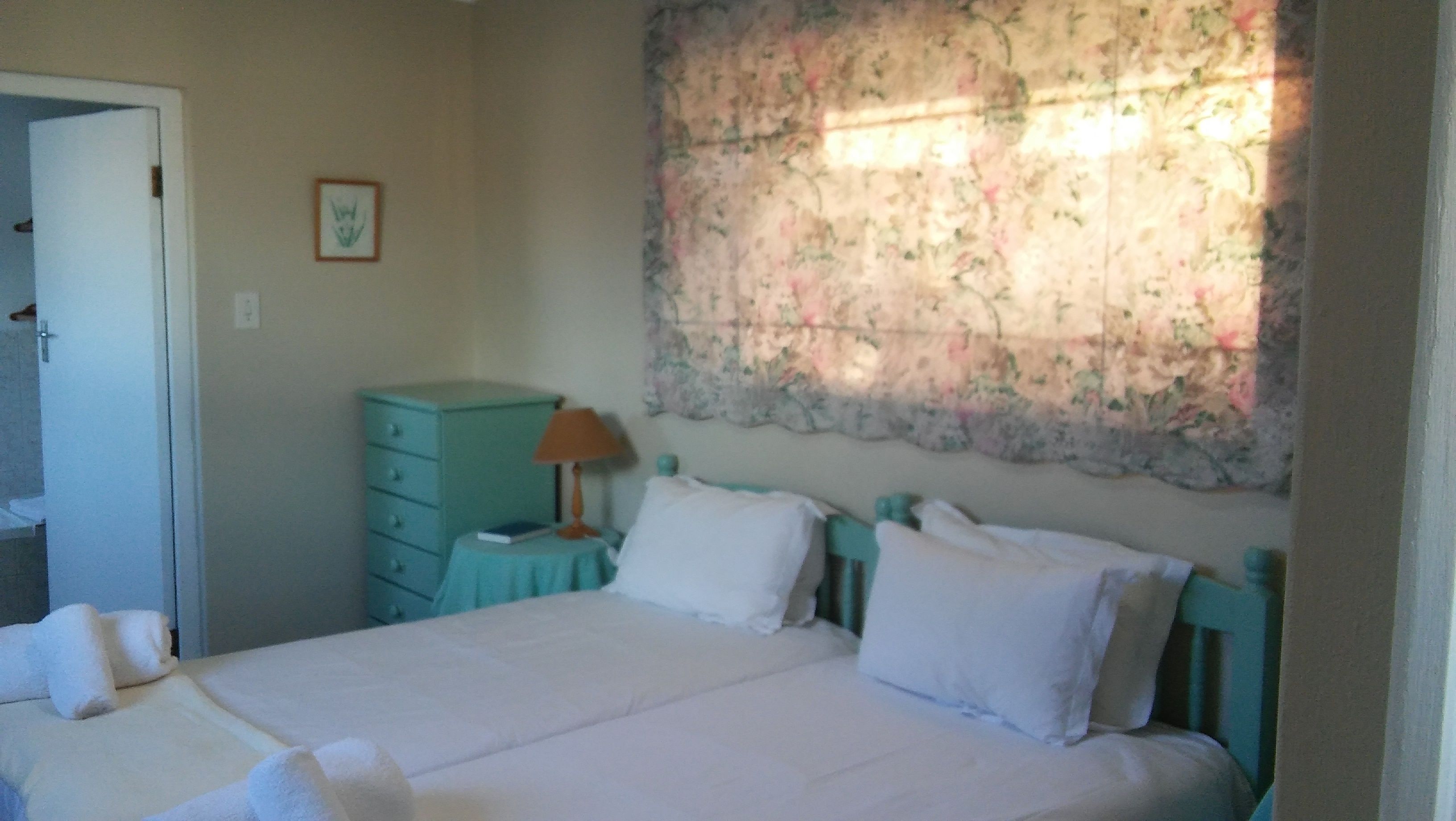 Un dormitorio con cama, cómoda, lámpara y un tapiz floral.