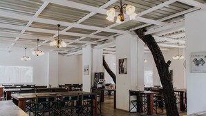 Un restaurant spacieux avec de hauts plafonds, des poutres apparentes et des luminaires suspendus. Les tables et les chaises sont disposées pour accueillir les clients.