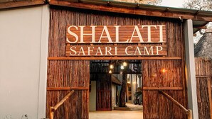 L’entrée du Shalati Safari Camp, avec sa façade en bois et un chemin de pierre qui y mène.