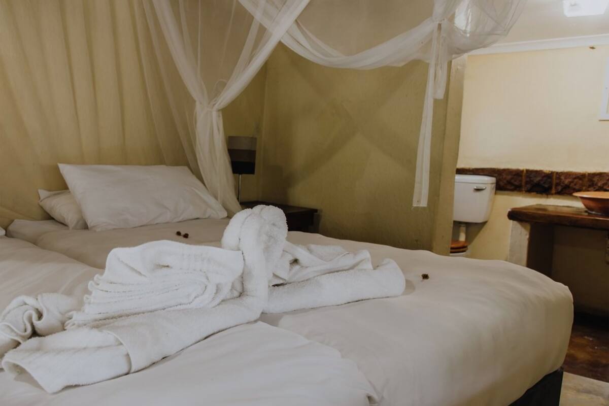 Habitación de hotel con cama, mesita de noche y baño visible a través de una puerta abierta.