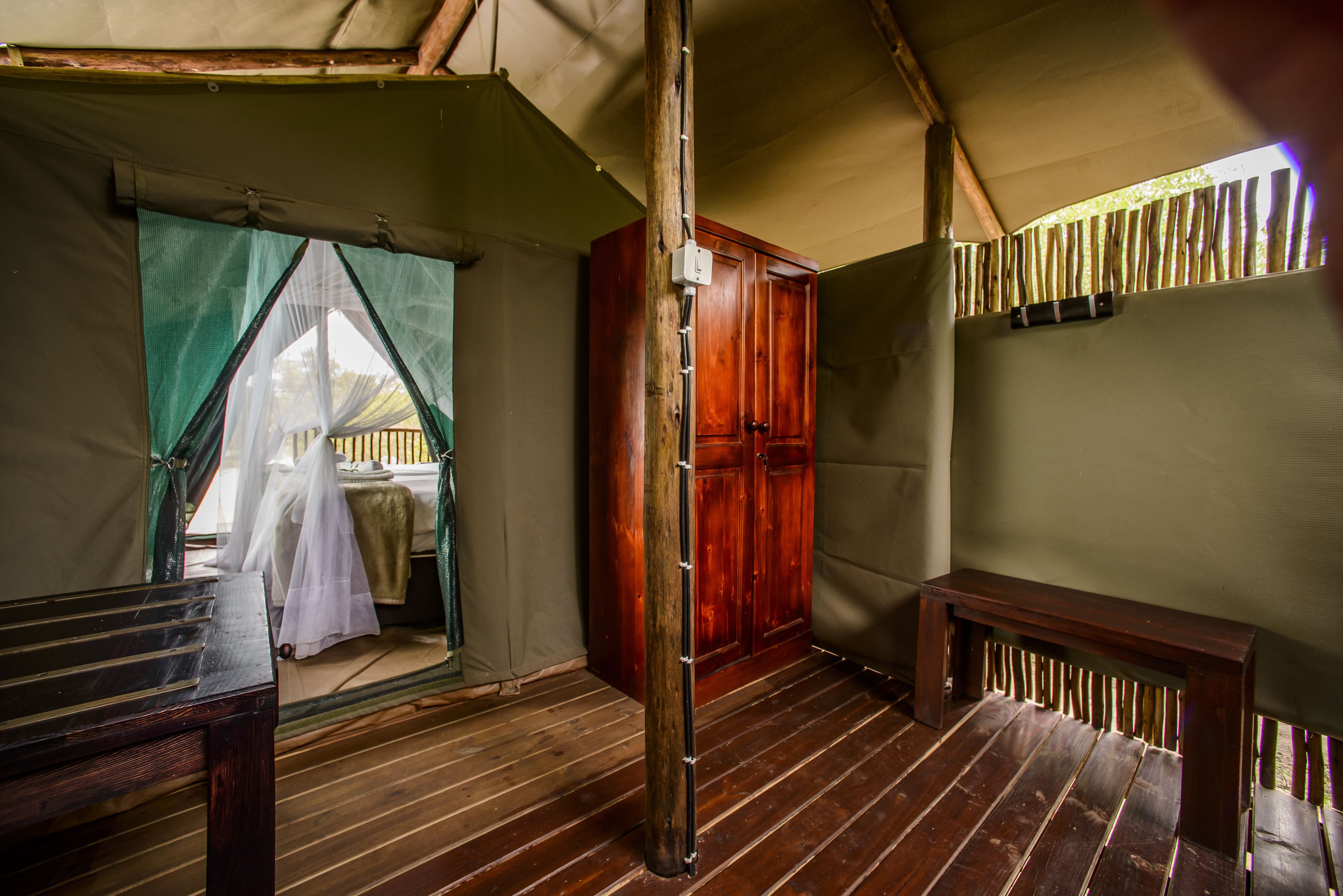 A tented room with a wooden bench, a wooden door, and a bench under a window.