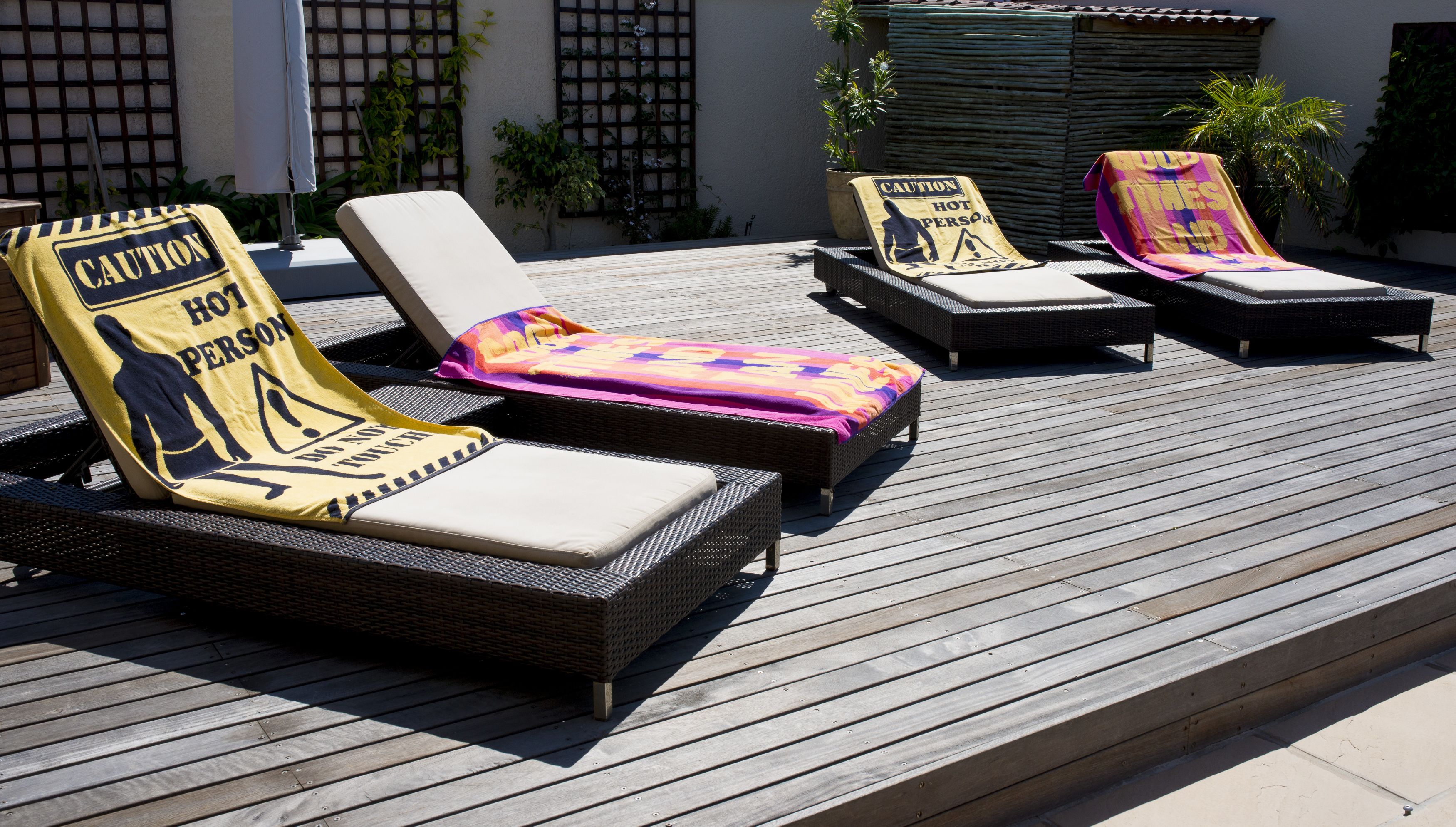 A poolside area with wicker lounge chairs, some with caution signs, and a wooden deck.