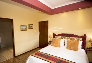 A hotel room with a large bed, wooden headboard, and a decorative bed runner.