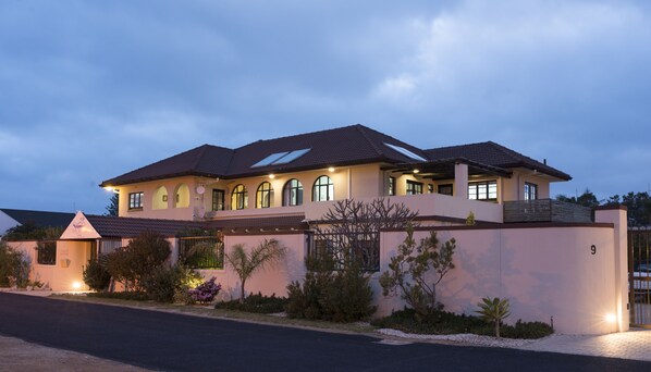 A large, two-story house with a flat roof, multiple windows, and a gated entrance.