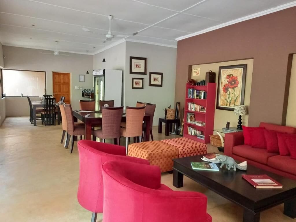 A spacious living room with a red sofa, a coffee table, and a bookshelf. There is a dining area with chairs and a table in the background.