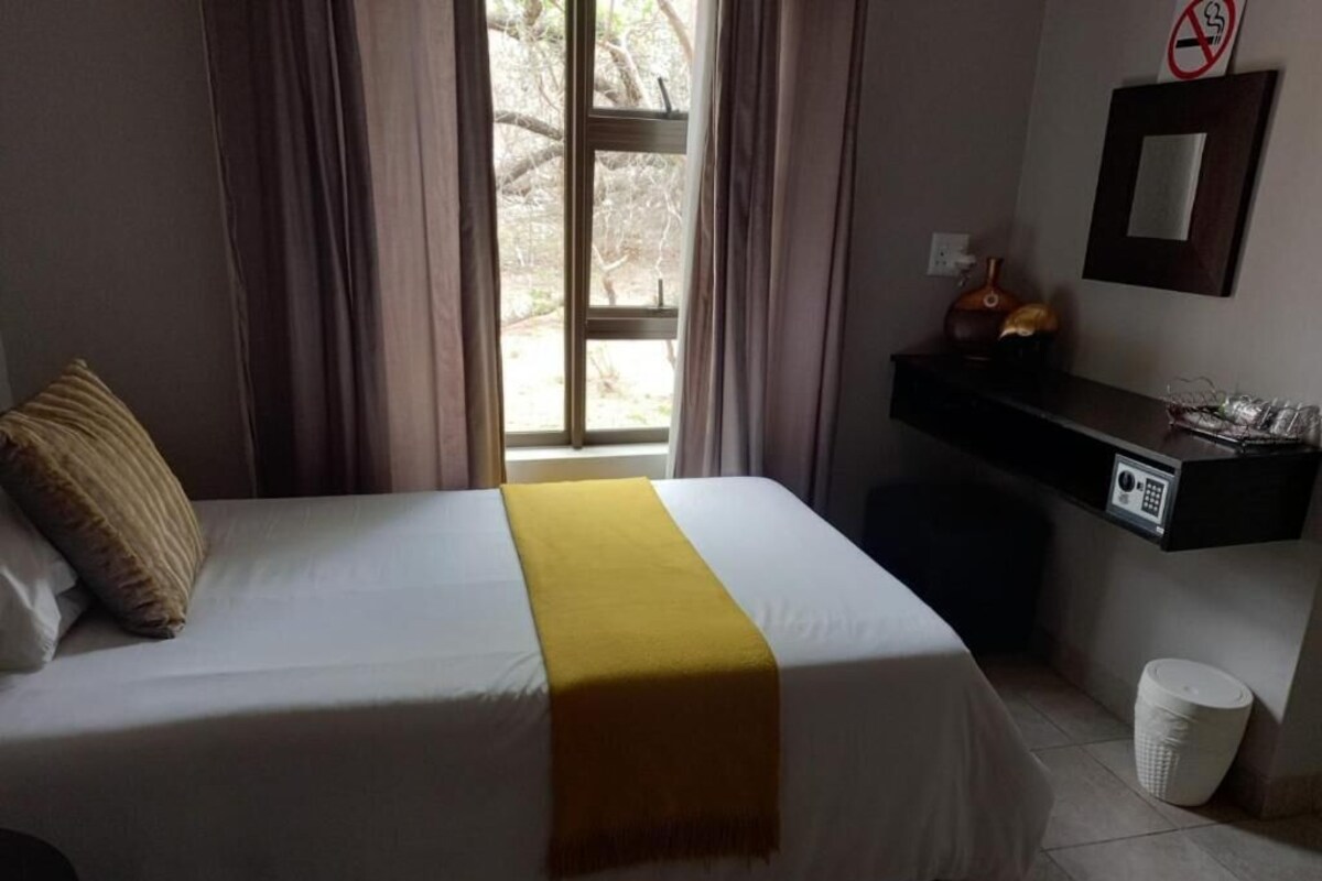 Hotelkamer met een bed, bureau, stoel, raam met gordijnen en een rookvrij bord aan de muur.