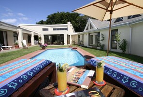 Zona de piscina con piscina, sillas de descanso y una sombrilla.