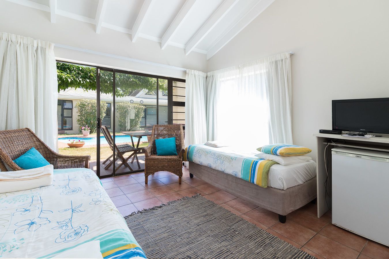 Una habitación con cama, una silla, un escritorio con televisor y vista a una piscina.