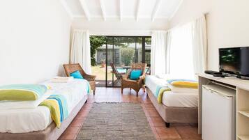 A hotel room with two single beds, a TV, a desk, and a view of a pool and garden.