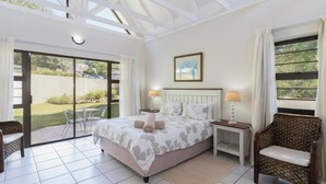 Une chambre avec un grand lit, deux tables de chevet, une chaise et une vue sur l’extérieur.