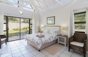 Un dormitorio con una cama grande, dos mesitas de noche, una silla y vistas al exterior.