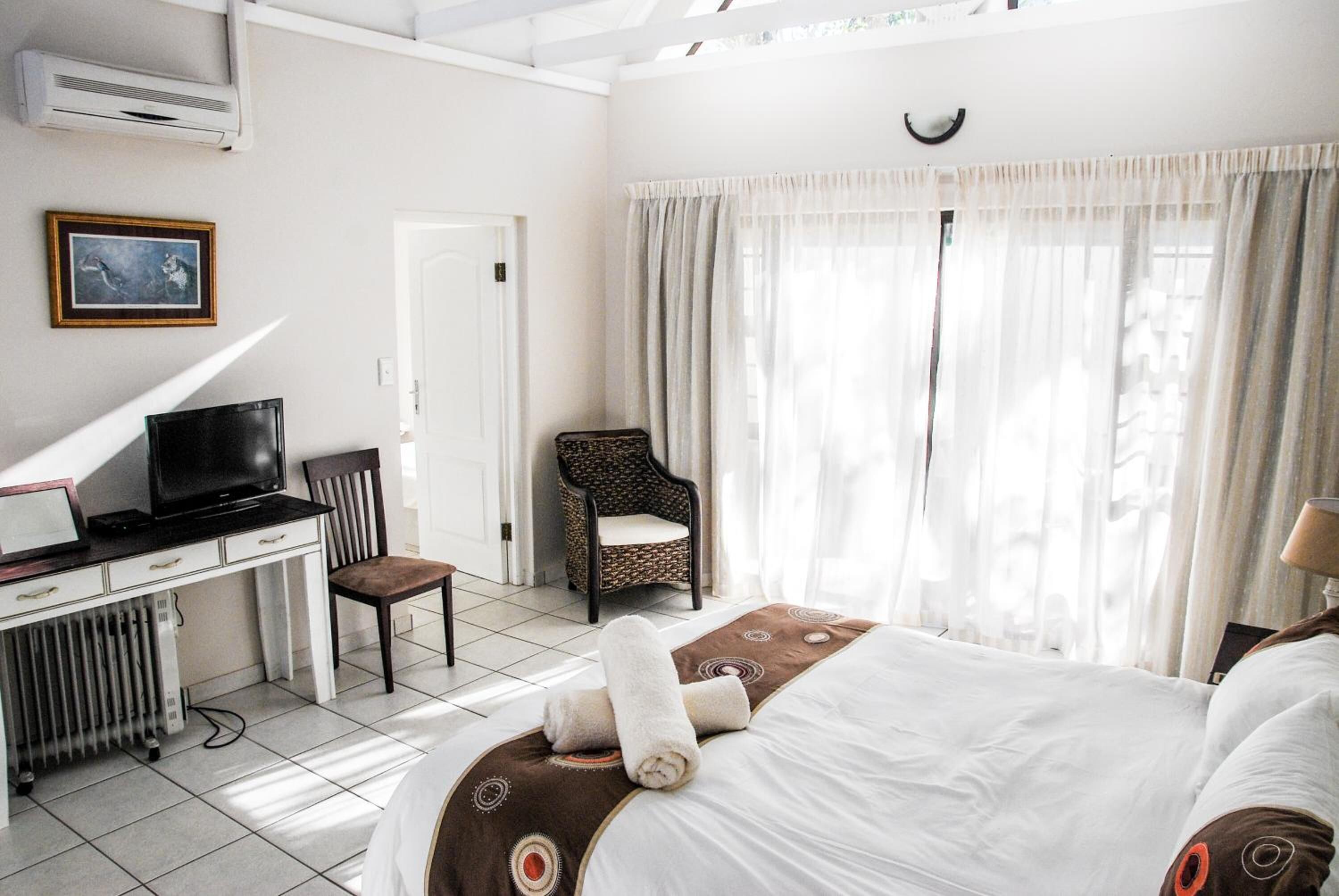 A hotel room with a bed, a desk with a computer, a chair, and a television.