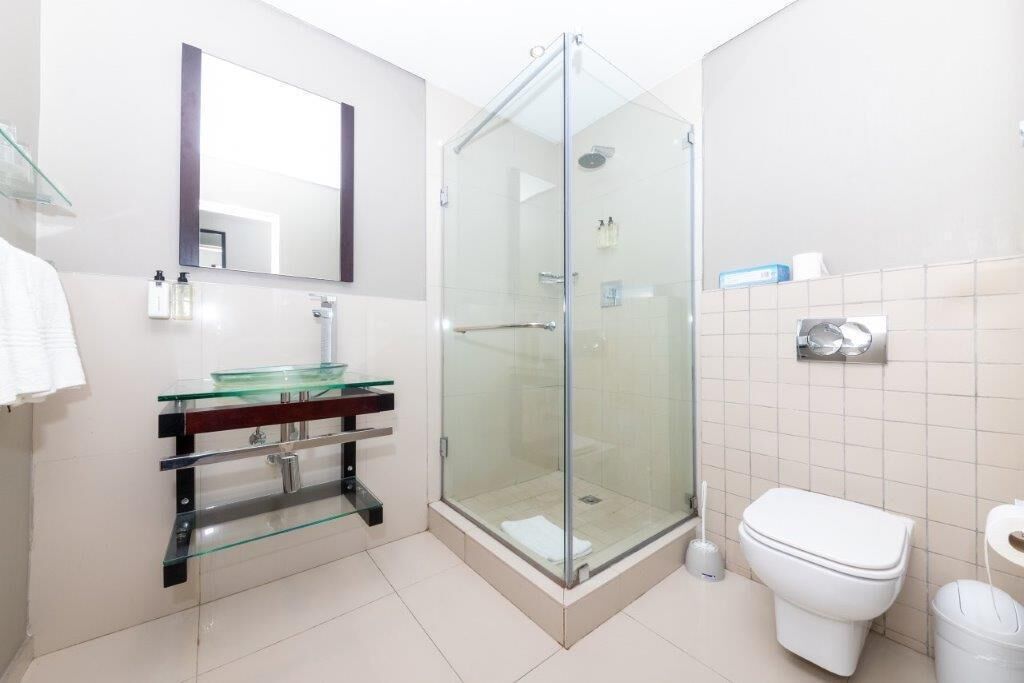 Um banheiro moderno com box de vidro, vaso sanitário branco e pia de vidro sobre bancada de madeira.