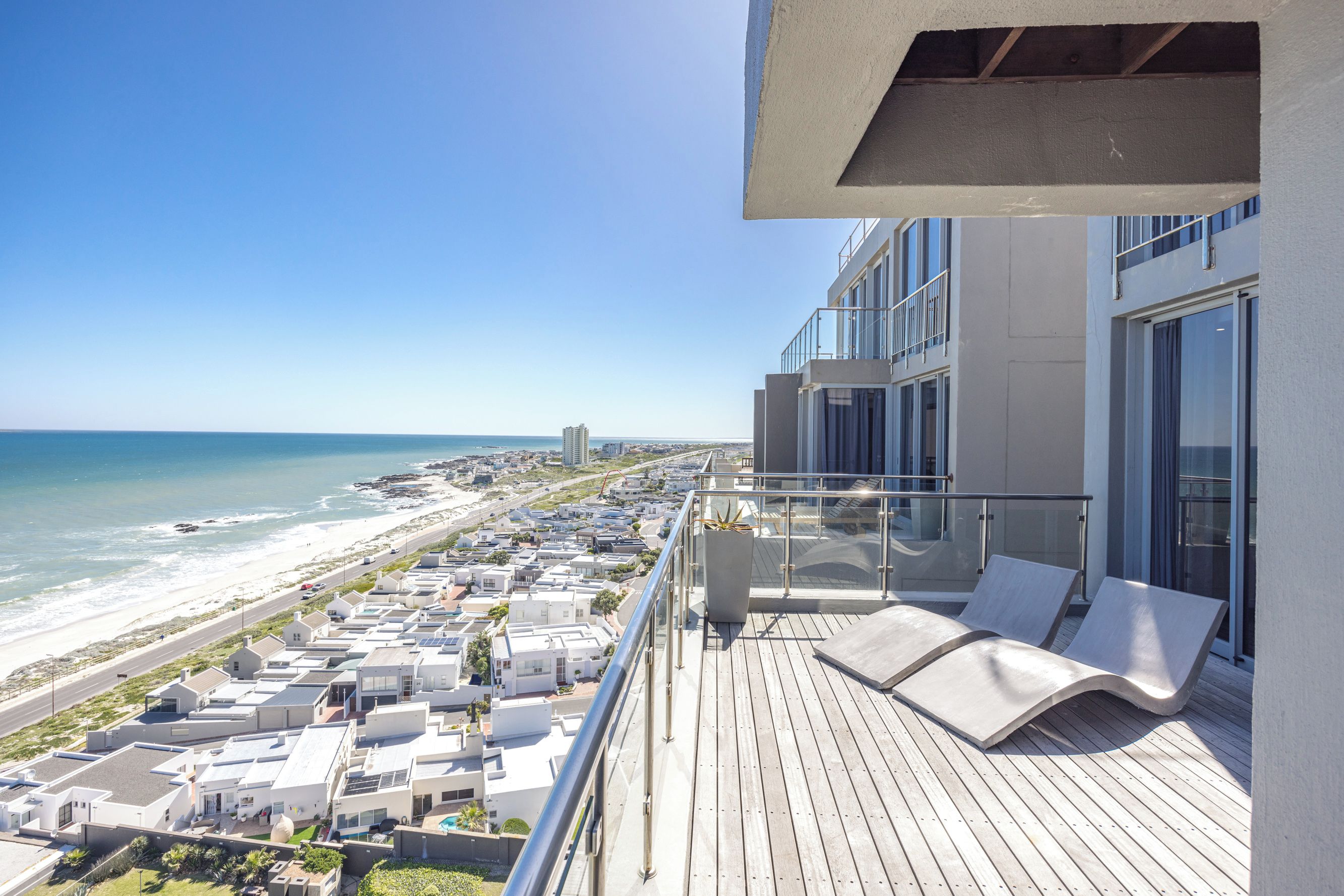 Un balcon avec vue sur la plage et l’océan, une terrasse en bois et des chaises longues.